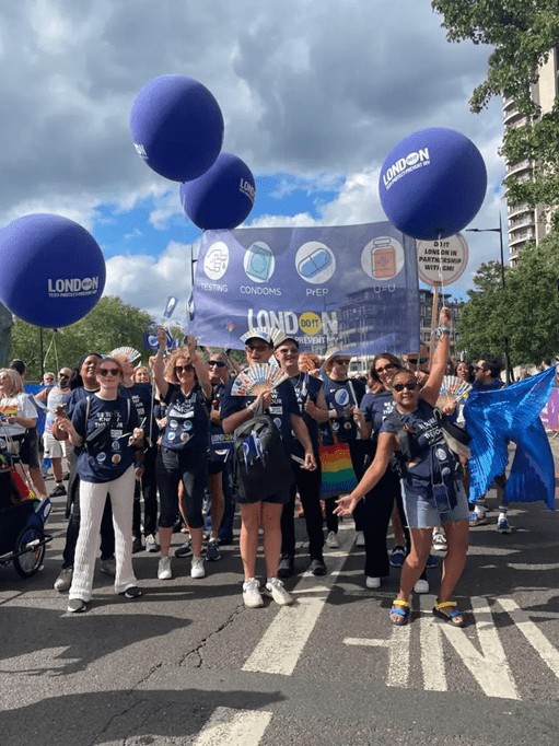 A group of people stand in front of a Do It London banner and balloon during London Pride March 2023