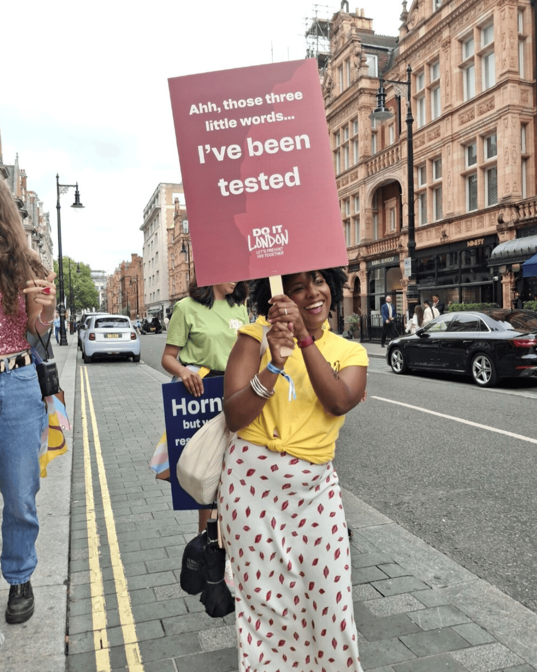 Black Londoner carries a placard for London Pride, which reads "Ahh those three little words... I've been tested"